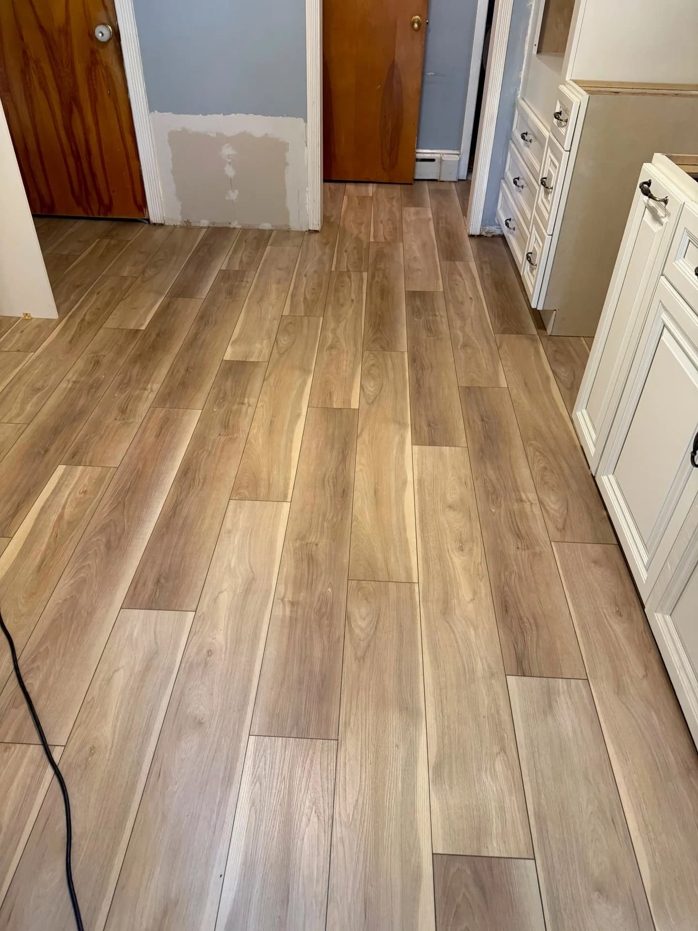 Light wood-look laminate flooring running through the Farmington kitchen beside white cabinets and two doorways.