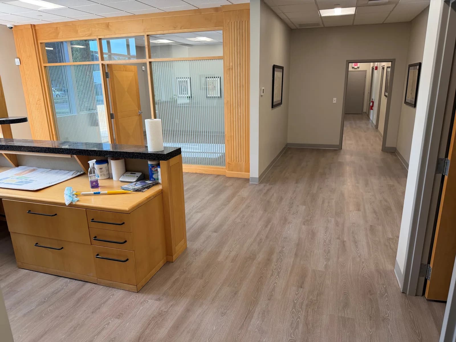 Completed wood-look LVP around the Hartford reception counter and continuing through the hallway, with cove base along the walls.