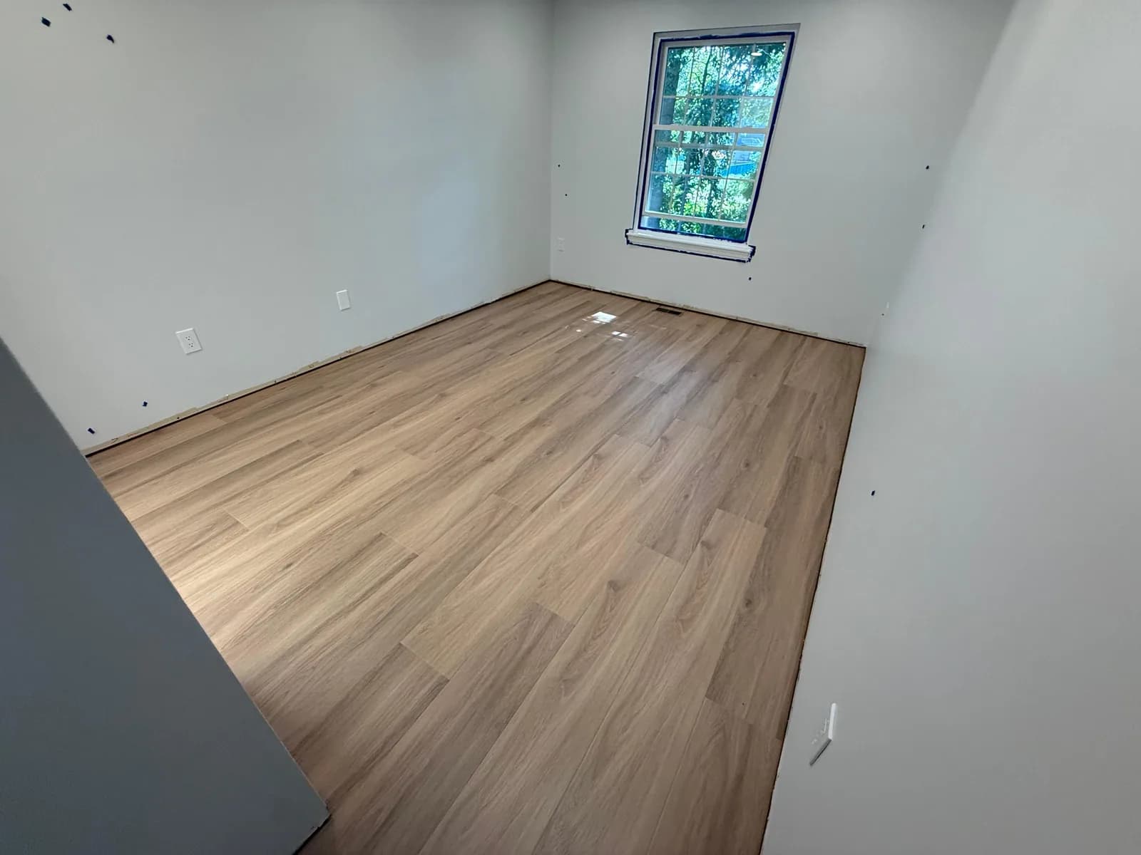 Light wood-look LVP installed across an empty room in Plainville, with baseboards still off and a floor vent beside the window.