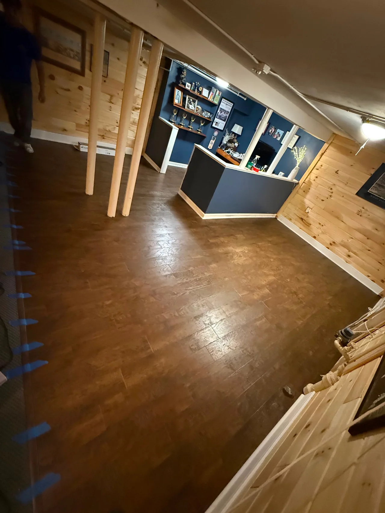 Brown plank flooring fitted around support posts and a counter in a lower-level room.