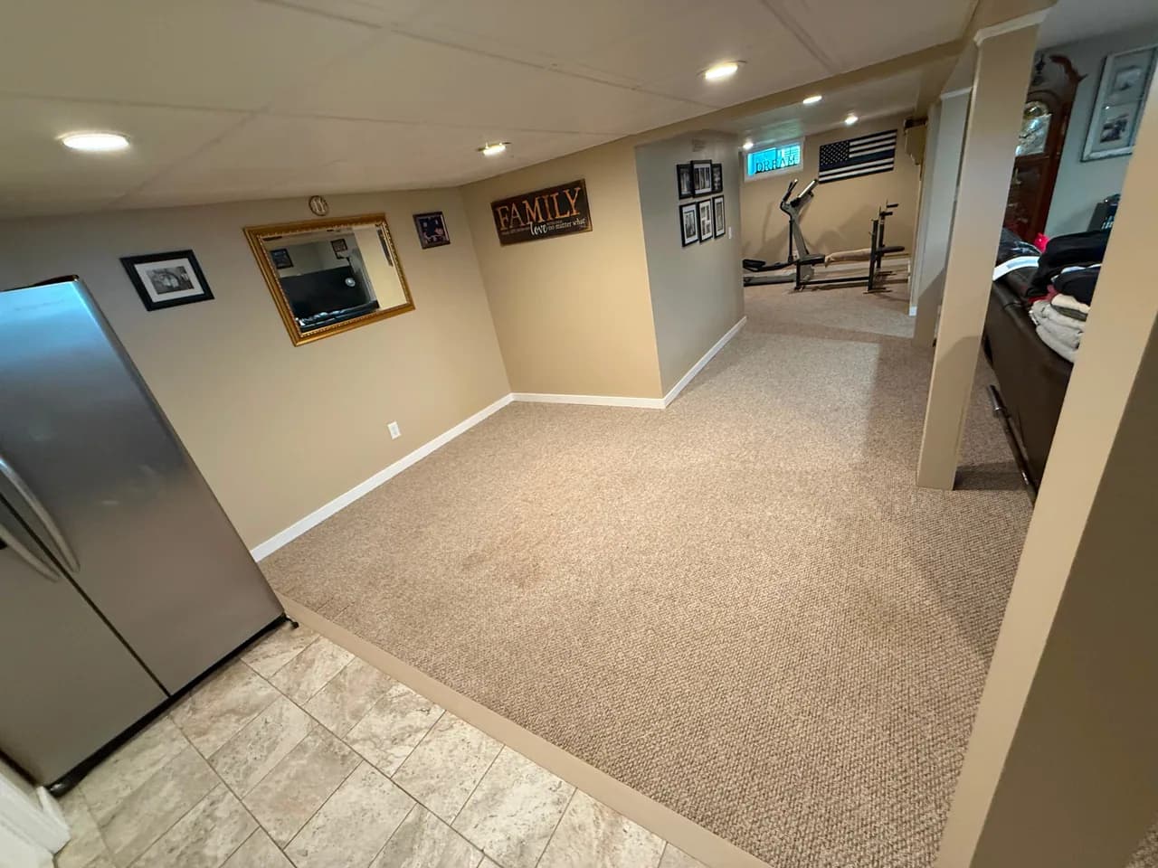Carpeted basement living area and hallway beside a tiled doorway transition.