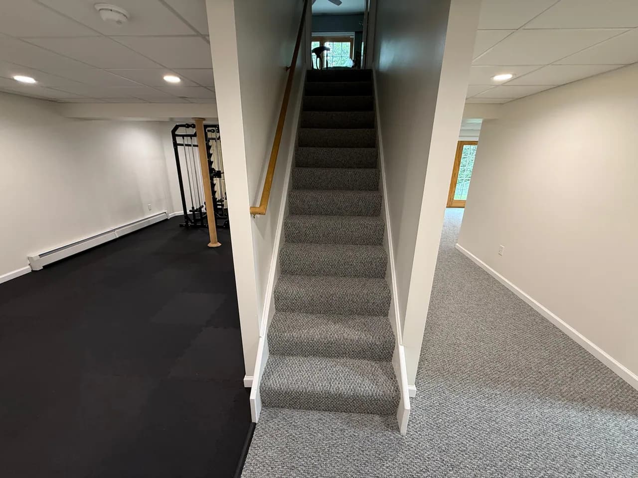 Gray carpet covering basement stairs and the adjoining room beside a home gym.