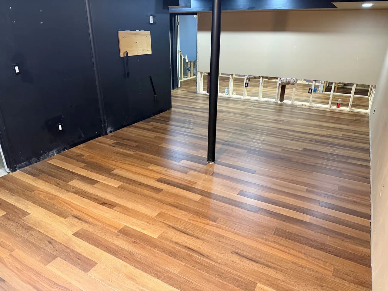 Luxury vinyl plank flooring fitted around a support column in a basement renovation.