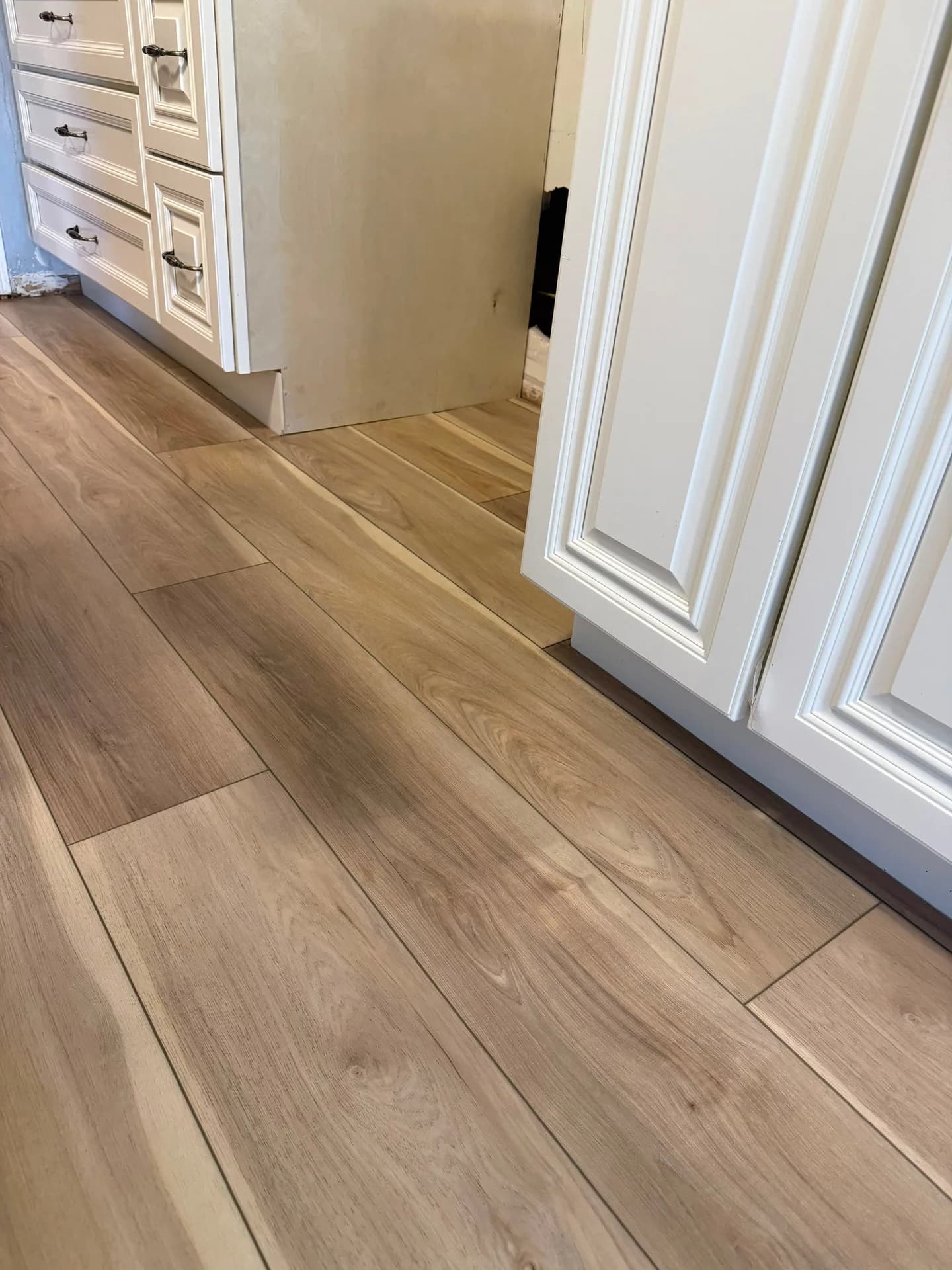 Laminate flooring fitted around white kitchen cabinet bases and the edge of an appliance opening in Farmington.