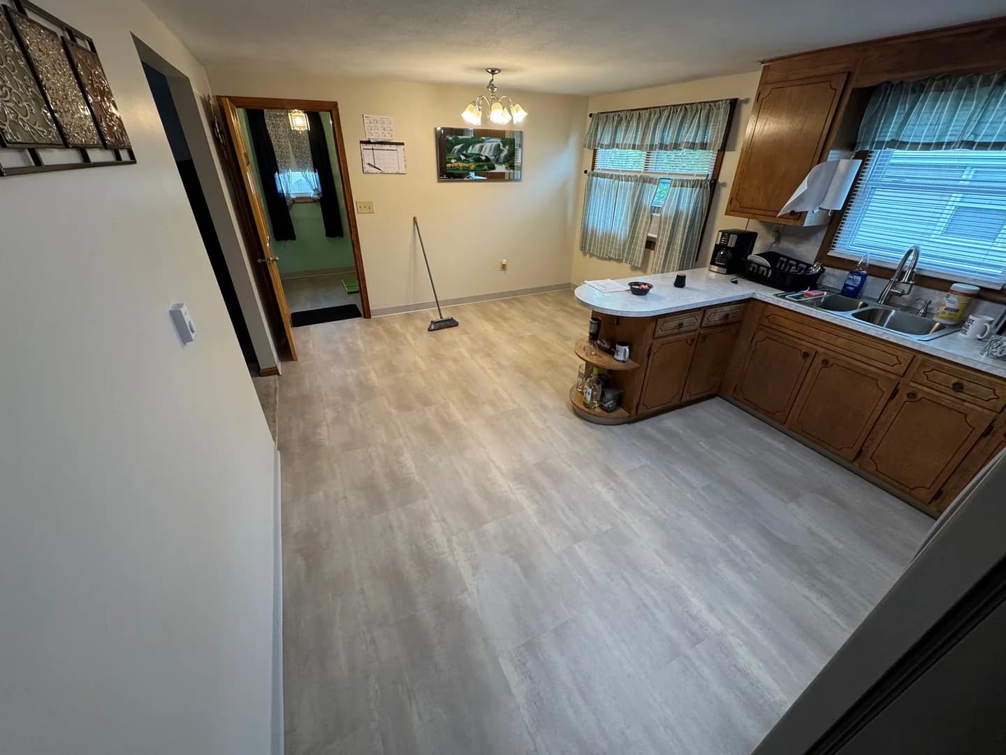 Light gray stone-look LVT across a New Britain kitchen beside wood cabinets, a curved counter end, and an adjoining doorway.