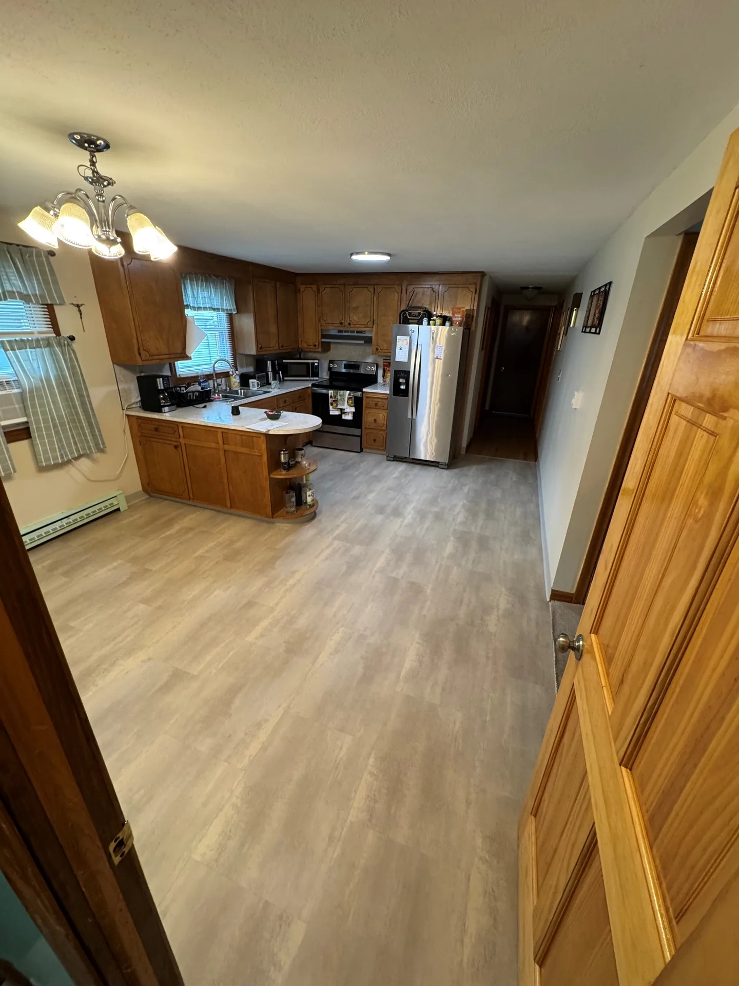 View through the kitchen doorway showing light gray LVT extending toward the refrigerator, stove, and rounded counter in New Britain.