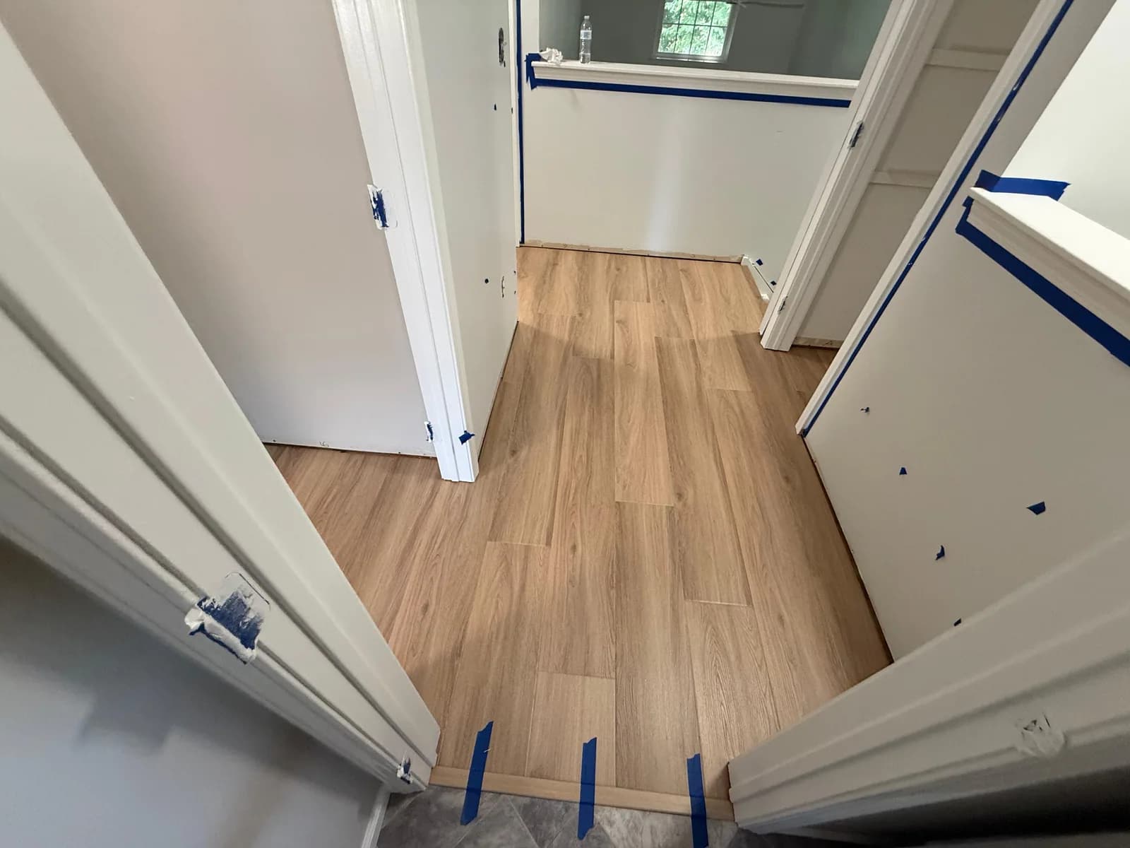 Light wood-look LVP fitted around hallway door frames beside a half wall, with taped threshold trim at the adjoining floor.