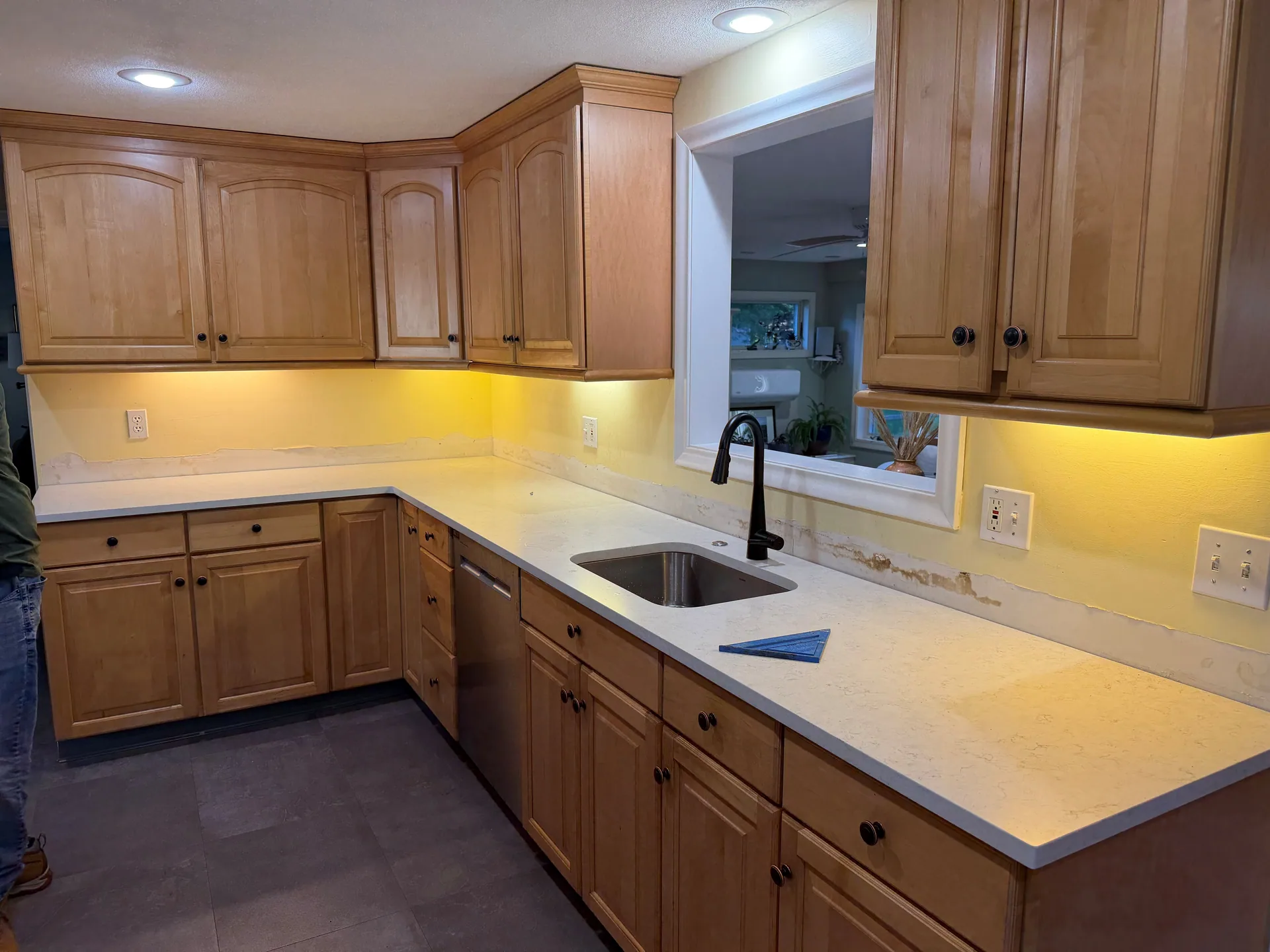 Kitchen before tiling, with exposed painted wall areas above an L-shaped countertop and beside the sink.