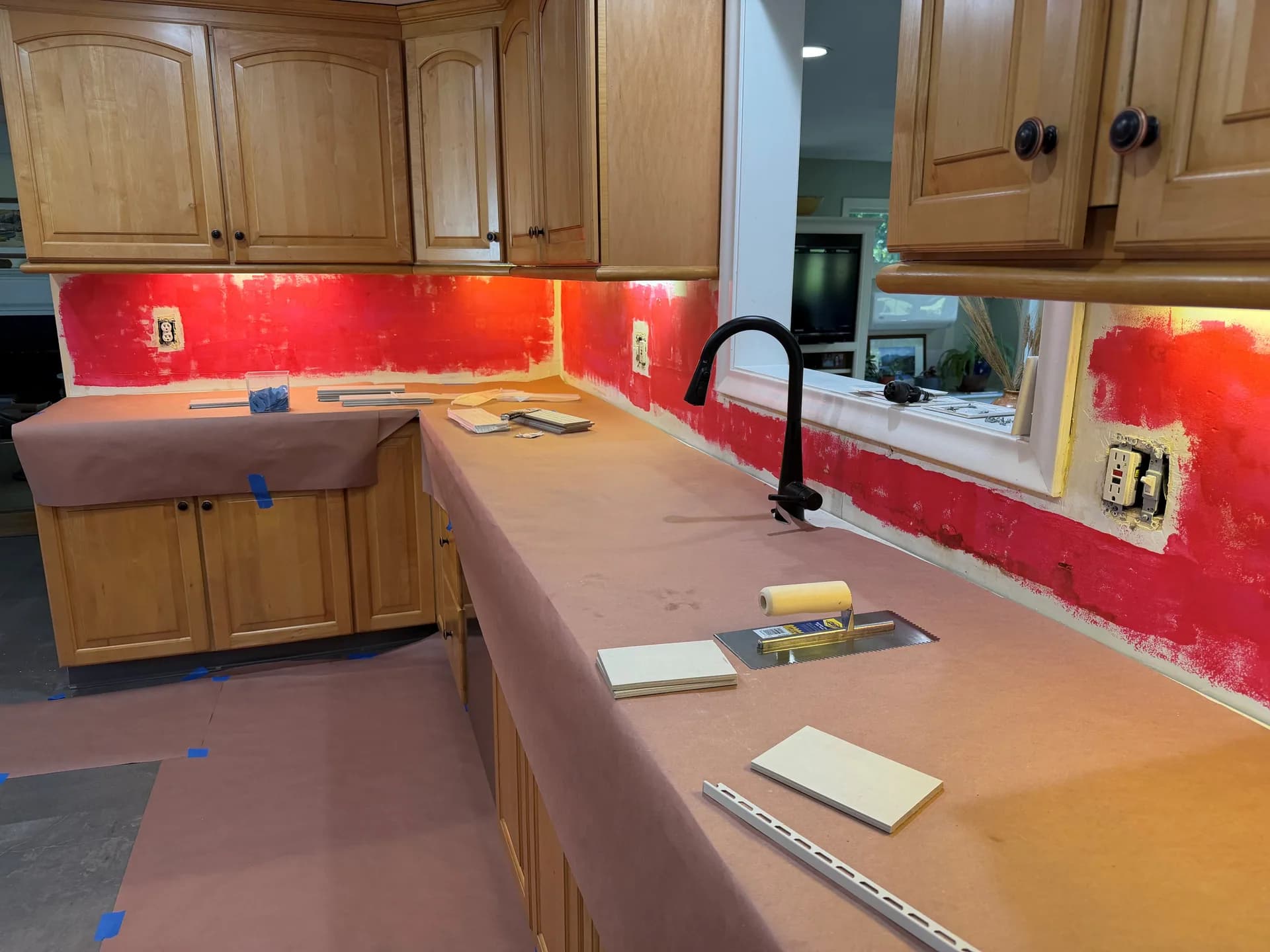 Red-coated wall areas behind the sink and paper protecting the counters before tile setting.