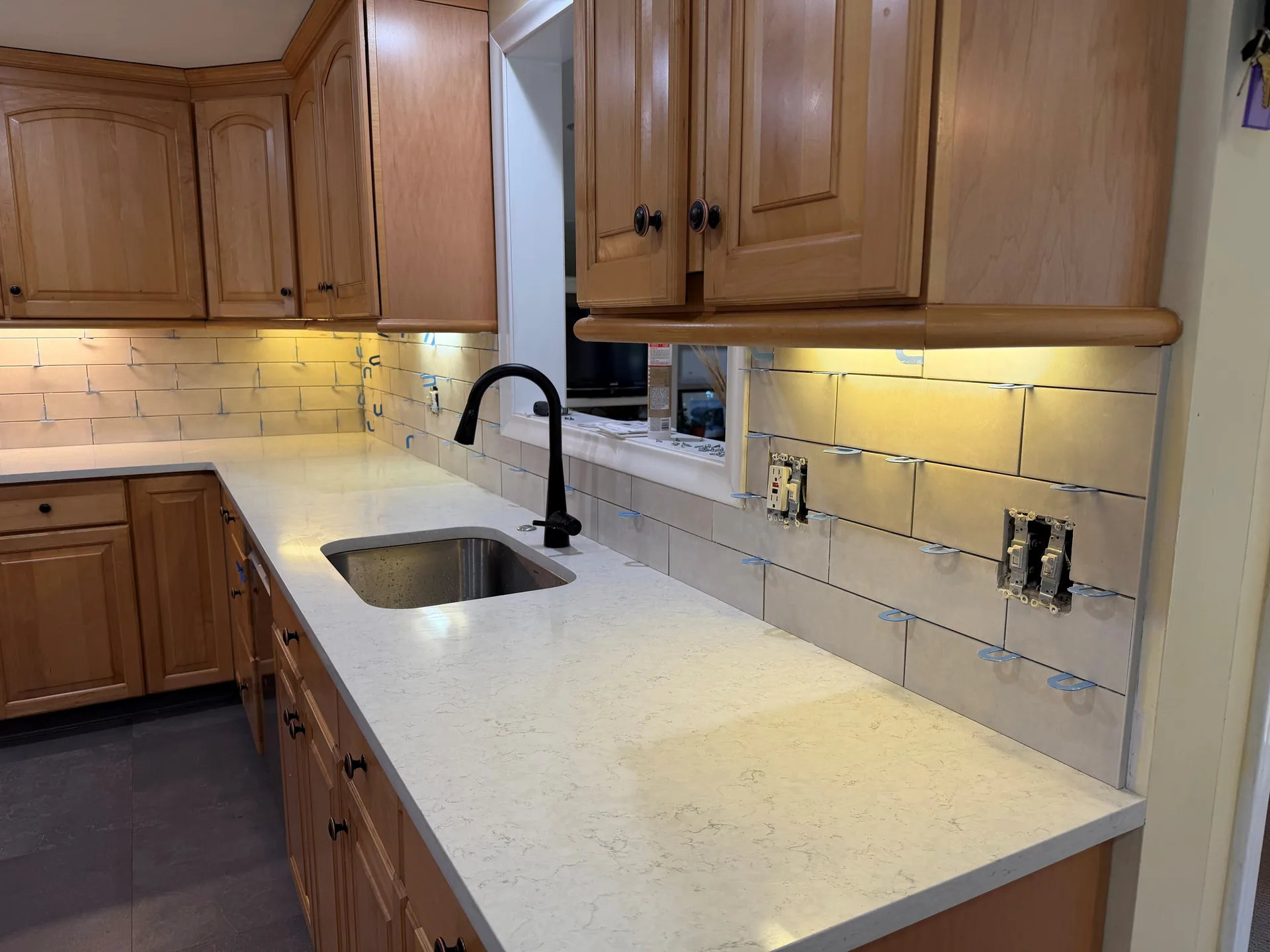 Spacers between backsplash tiles around the sink, pass-through trim, and switch openings.
