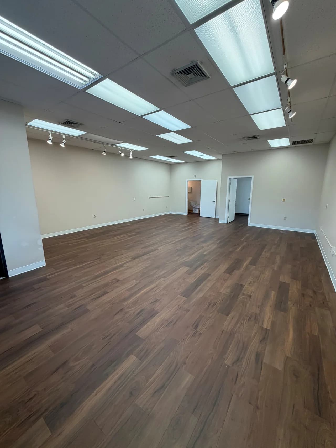 Wood-look plank flooring across an open commercial room and adjoining doorways.